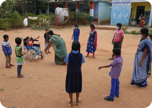 Children playing outdoors with adults in a sandy area near a school.