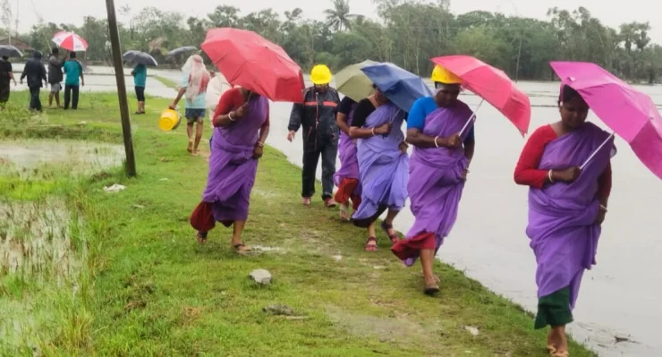 People with umbrellas walking along a wet path beside a flooded area.