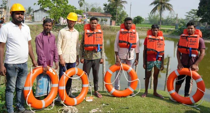 Group of men wearing life jackets and holding lifebuoys beside a waterway.