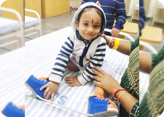 A child in a striped outfit with an orthopedic device on a hospital bed, assisted by adults.