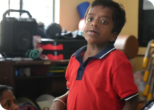 Person in red shirt standing in a room with household items and a speaker in the background.