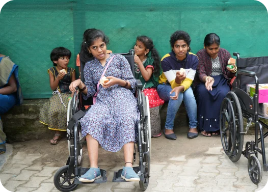 Group of people sitting outside, one in a wheelchair, with snacks and drinks in hand.