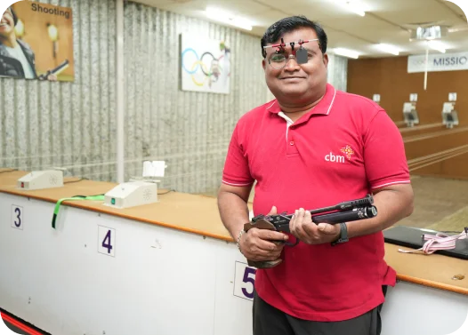 Person in a red shirt holding a pistol in a shooting range.