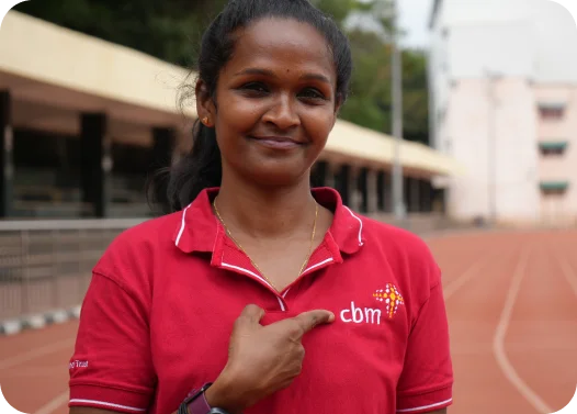 Person in a red polo shirt with Cbm logo, standing on a running track.