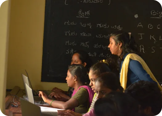 Students using a laptop in a classroom with a blackboard in the background.