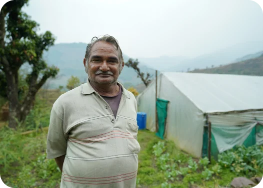 Person in a polo shirt standing in front of a greenhouse with hills in the background.